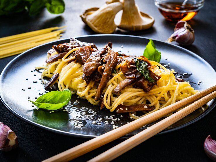 Ein schwarzer Teller mit Pasta mit Sojabutter und Pilzen neben frischen Zutaten