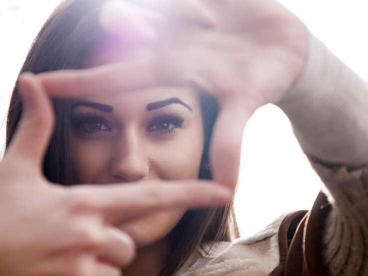 Frau legt Fokus auf ihre Augen, indem sie  mit ihren Fingern drumherum ein Rechteck zeigt