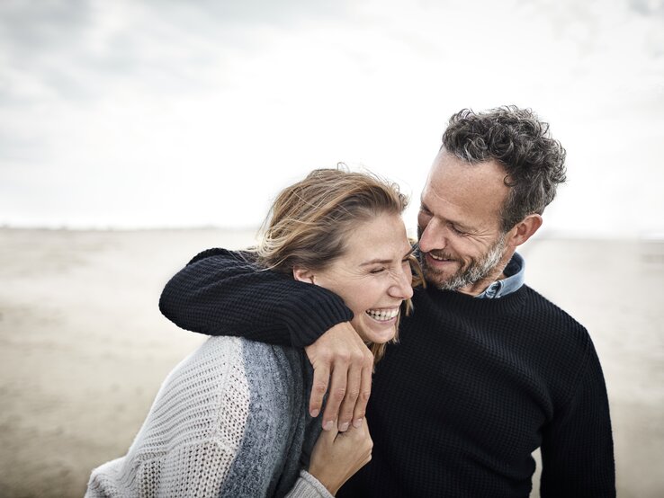 Zwei Menschen am Strand lachen miteinander. 