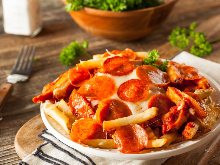 Pommes überbacken mit Salami auf hölzernem Untergrund. 