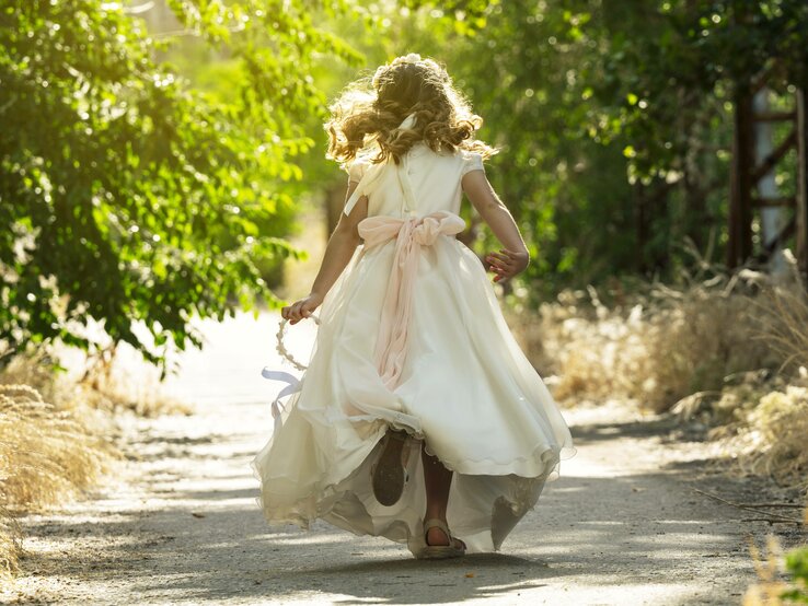 Ein Kind läuft in einem weißen Kleid einen Waldweg entlang
