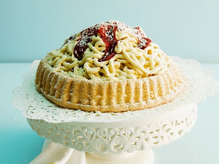 Auf einem Tortenteller steht eine Spaghettieistorte. Sie ist mit Johannisbeergelee und Puderzucker überzogen. 
