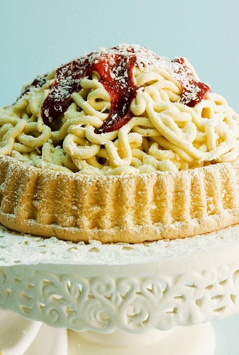 Auf einem Tortenteller steht eine Spaghettieistorte. Sie ist mit Johannisbeergelee und Puderzucker überzogen. 
