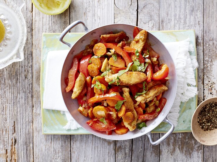 Ein schneller Hähnchen-Wok mit sautiertem Gemüse, abgelöscht mit Sojasauce und garniert mit frischem Koriander und Zitronensaft, serviert im Wok auf einem hellen Holztisch. 