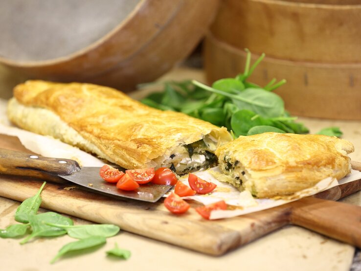 Spinat-Strudel mit Feta und Knoblauch / Holzbrettchen / Untergrund Holz / frische Basilikumblätter, Tomaten