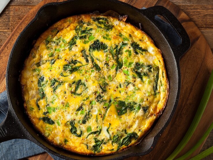 Eine gusseiserne Pfanne mit der Frittata auf einem dunklem Holztisch.