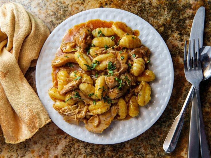 Gnocchi mit Gulasch auf weißem Teller, angerichtet auf Marmoruntergrund.