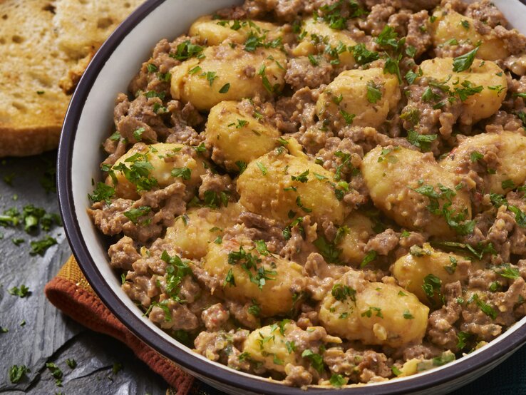 Gnocchi-Pfanne mit Schmand-Hackfleisch auf weißem Teller mit braunem Rand. Das Ganze steht auf einer Schieferplatte.