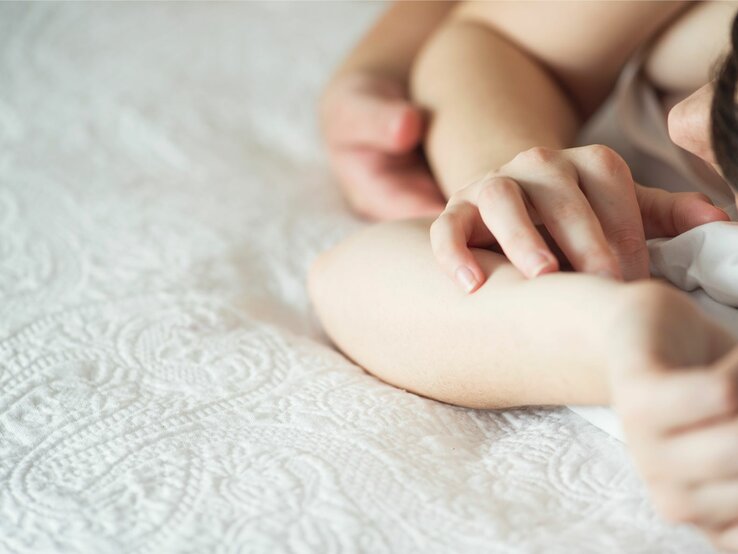 Paar liegt zusammen im Bett. Zu sehen ist seine Hand, die auf ihrer Hand liegt.