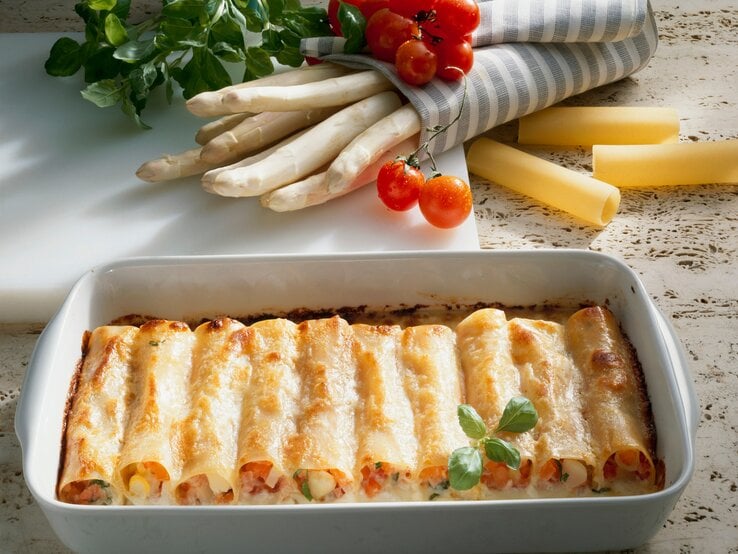 Spargel-Cannelloni in weißer Auflaufform. Daneben einige Zutaten.