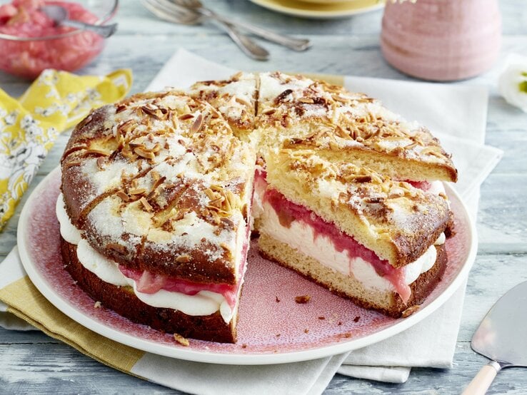 Auf einem Teller ist ein gefüllter Rhabarber-Butterkuchen angerichtet. Er ist mit Puderzucker bestreut.