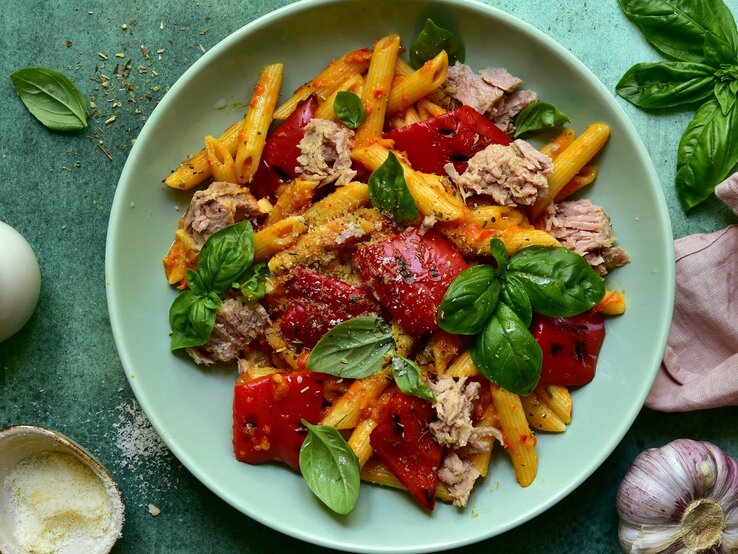 Ein grüner Teller mit der Penne an Thunfisch-Tomatensoße auf einem grünen Untergrund. 