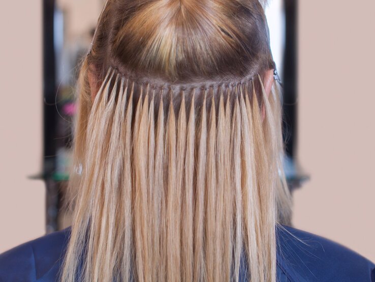 Haarverlängerung Hinterkopf einer Person mit einer speziellen Frisur. Zu sehen sind Extensions, die mittels der Tape-in-Methode befestigt wurden.