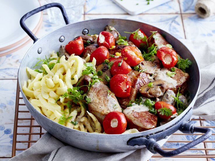 Spätzle-Jägerpfanne mit Pilzen, gerösteter Papika und frischer Petersilie, serviert in einer rustikalen tiefen Pfanne auf einem Keramiktisch. 