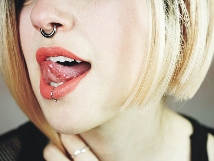Eine blonde Frau mit einem Septum- und einem Lippen-Percing streckt die Zunge raus. Sie hat kein Wildfleisch am Piercing.