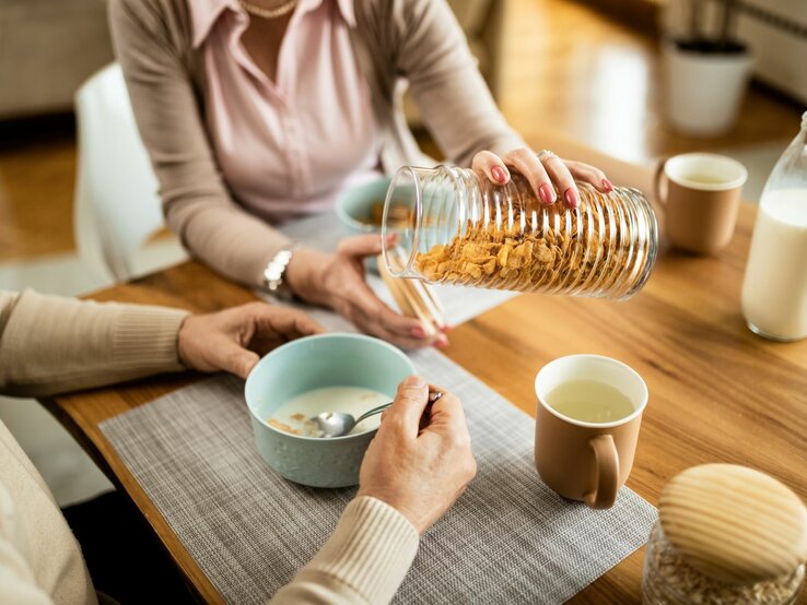 Eine Frau schüttet ihrem Mann am Frühstückstisch Cornflakes in eine Schale