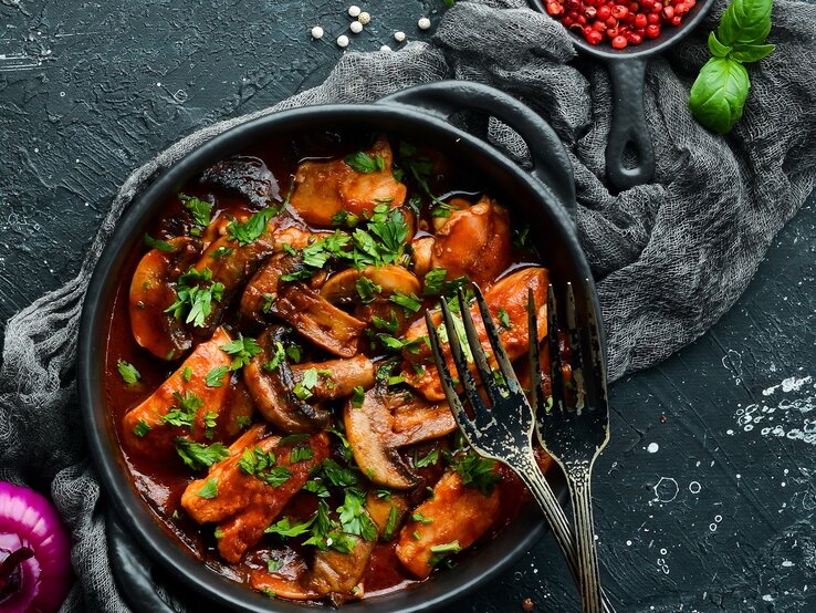 Blitz-Gulasch Eine schwarze Schale mit dem Blitz-Gulasch auf einem dunklen Tisch mit rotem Pfeffer und Basilikum im Hintergrund.