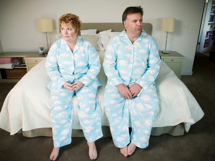 Was tun, wenn man den Partner sexuell nicht mehr attraktiv findet | © Getty Images / Big Cheese Photo Ein reiferes Paar sitzt im Pyjama nebeneinander auf dem Bettrand und schaut etwas frustriert in die jeweils andere Richtung | © Getty Images / Big Cheese Photo