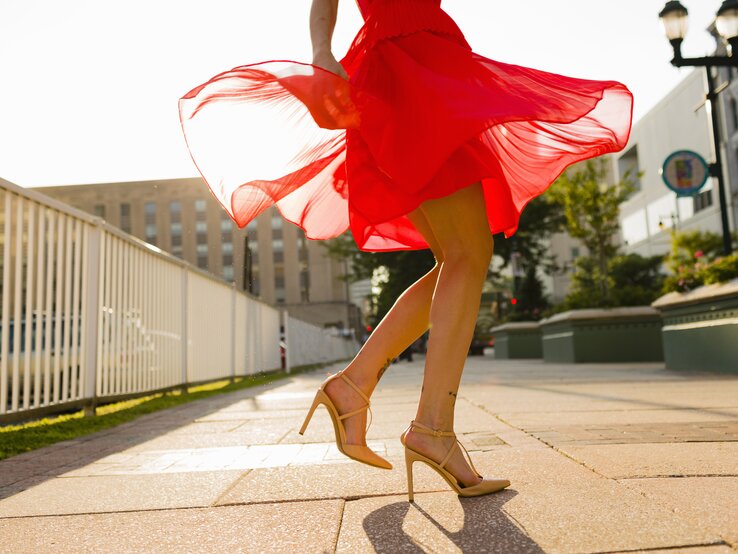 Junge Frau in hohen Schuhen und einem roten Kleid, das im Wind weht.