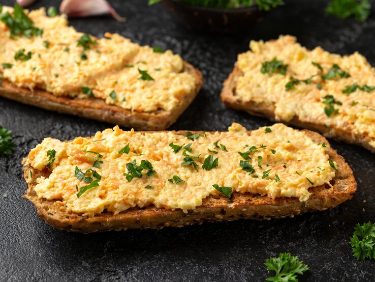 drei brote mit einem Käse-Karotten-Aufstrich liegen auf einem Tisch.