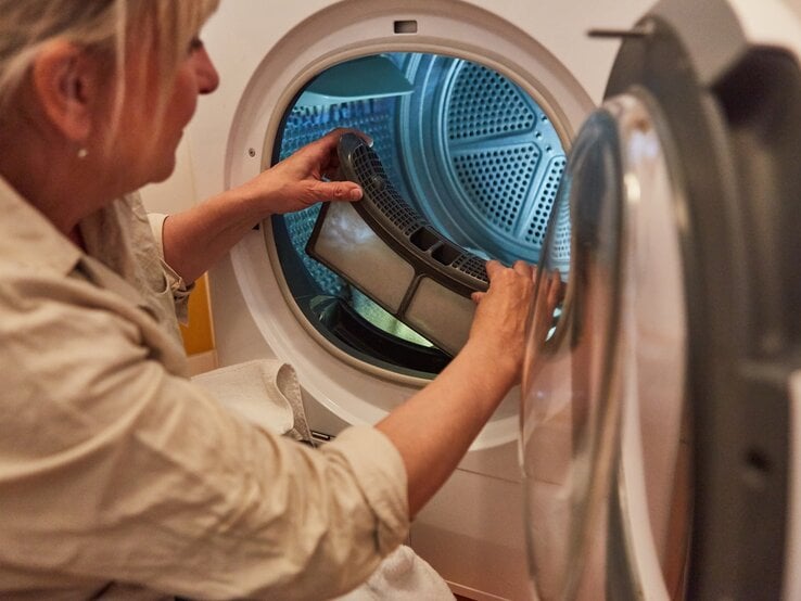 Hausfrau reinigt das Flusensieb von Wäschetrockner. 