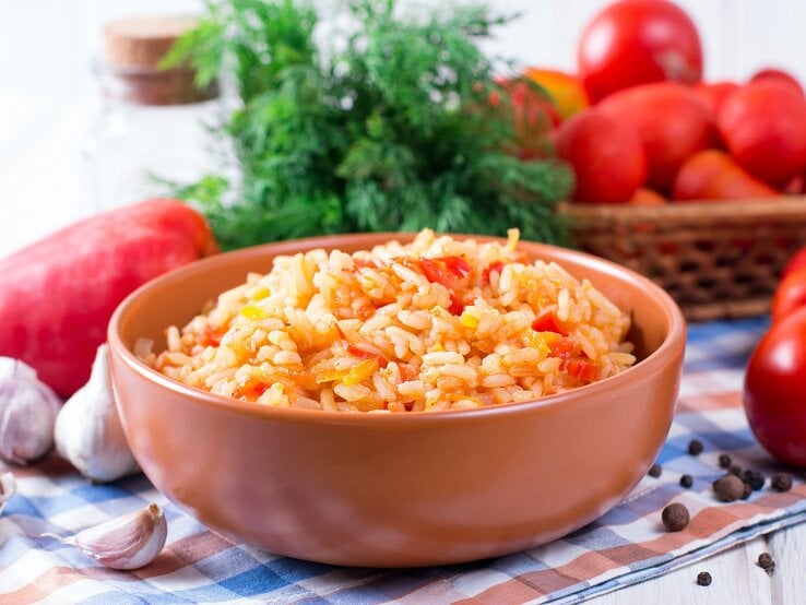 Eine Schale griechischer Tomatenreis mit Paprika, drumherum die frischen Zutaten.
