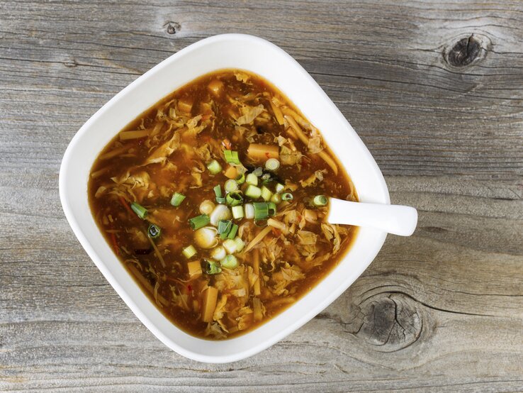 Ein weißer Teller mit der Kohlsuppe auf einem dunklen Holztisch.