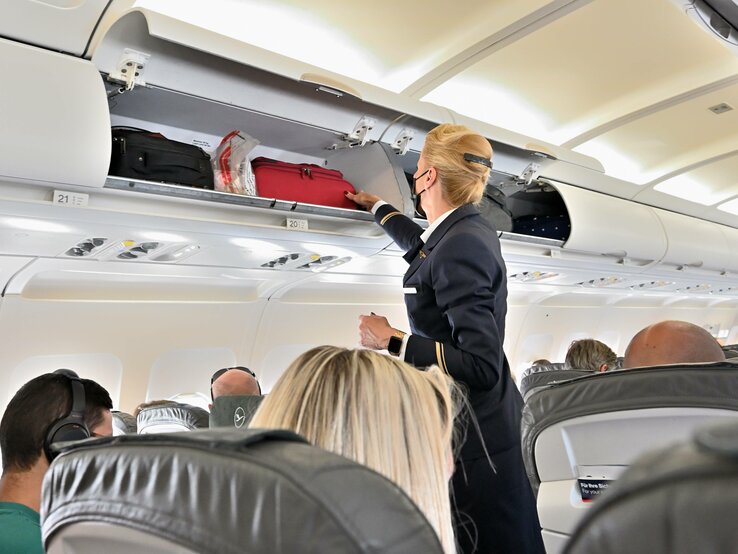 Eine Flugbegleiterin vor einem geöffneten Gepäckfach mit Handgepäck.