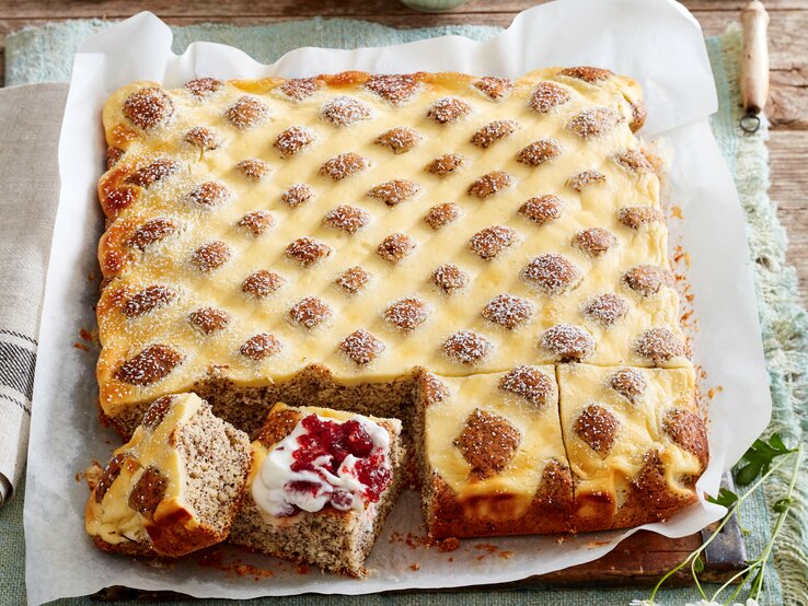 Steppdecken-Mohnkuchen, gebacken auf einem Blech und angeschnitten serviert mit Preiselbeer-Sahne und Puderzucker. 