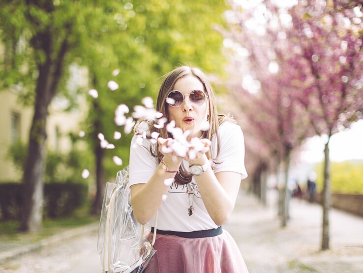 Eine Frau pustet Blüten aus ihren Händen in die Luft. | © iStock/Eva-Katalin