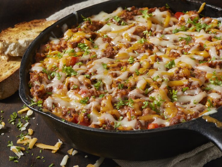 Italienische Hackfleisch-Reis-Pfanne mit frischen Kräutern und verlaufenem Käse in einer gusseisernen Pfanne.