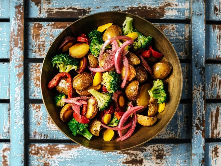 Unser Rezept des Monats: Gegrillter Kartoffelsalat mit Gemüse und Hirtenkäse Gegrillter Kartoffelsalat mit Gemüse, Hirtenkäse und rotem Pesto in Schale auf blauem Holz. Aufnahme aus der Vogelperspektive.