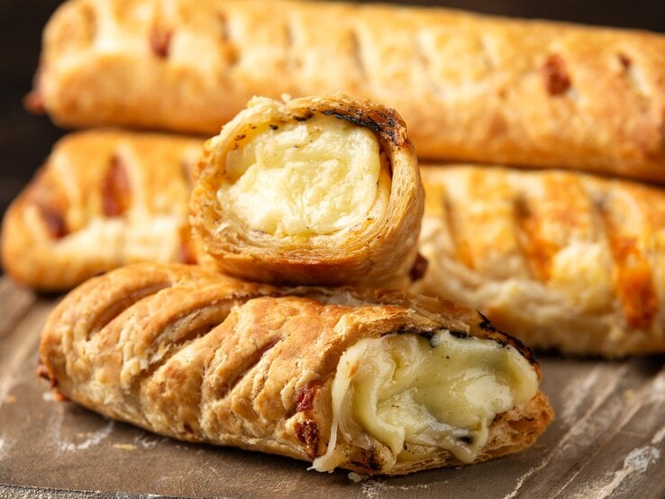 Unsere gefüllten Blätterteig-Brötchen mit Käse und Zwiebeln sind der ideale Snack für einen gemütlichen Fernsehabend oder auch für eine Party. Gefüllte Blätterteig-Brötchen mit Käse & Zwiebeln auf Holzbrett.