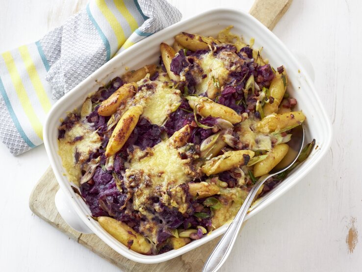 Rotkohl-Schupfnudel-Gratin mit Speck, serviert in einer hellen Auflaufform auf weißem Untergrund.