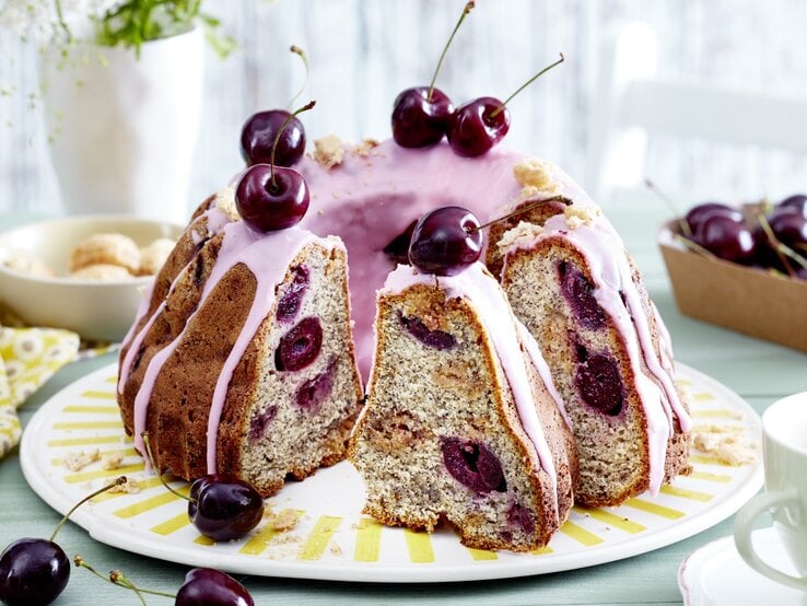 Ein Schmand-Mohnkuchen mit Kirschen auf einem weißen flachen Teller.