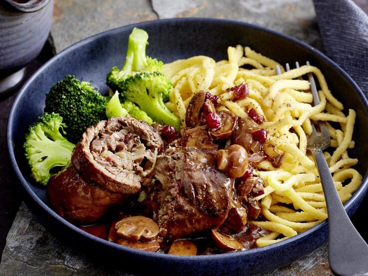 Unsere Rinderrouladen mit Pilzen und Spätzle sind ein richtiges Wohlfühlessen für die ganze Familie! Das musst du probieren.  Auf einem tiefen Teller liegt eine Portion Rinderrouladen mit Pilzen und Spätzle. Sie wird mit Brokkoli serviert.