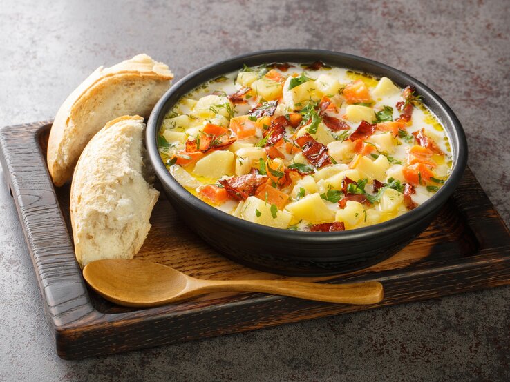 Polnische Kartoffelsuppe Kartoflanka mit Brot und Holzlöffel auf Holzbrett auf grauem Untergrund. Draufsicht.