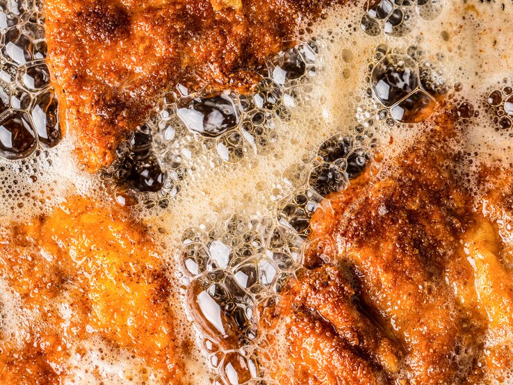 Brutzelnde Schnitzel in einer Pfanne mit heißem Fett.