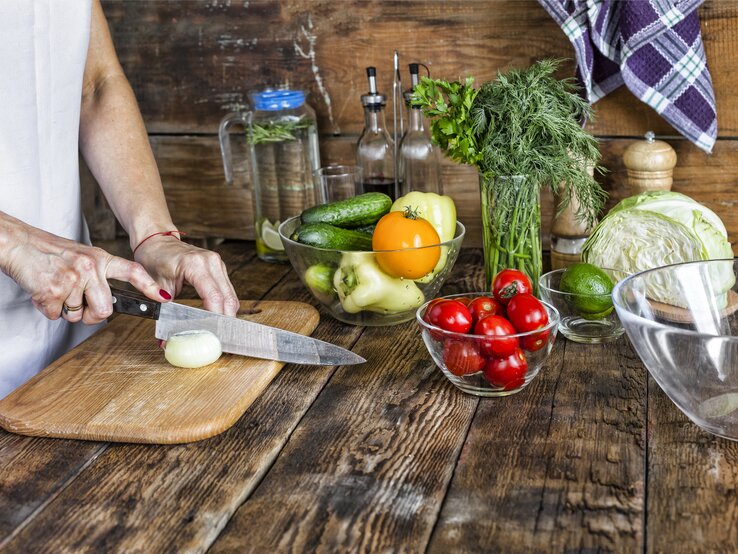 Eine Person schneidet Gemüse auf einem Holzbrett in einer rustikalen Küche.