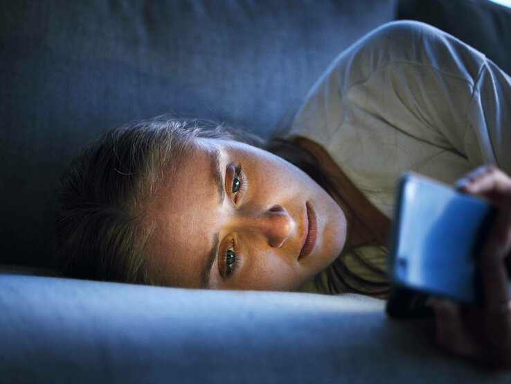 Frau liegt im Bett und starrt auf ihr Handy.