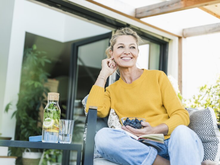 Frau sitzt mit Schale voller Blaubeeren auf einer Terrasse