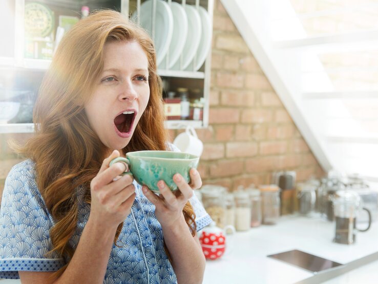 Frau gähnt mit großer Tasse in der Hand