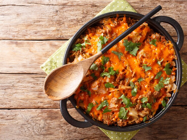 Kohlauflauf mit Hackfleisch und Cheddar in gusseiserner Pfanne auf Holztisch. 