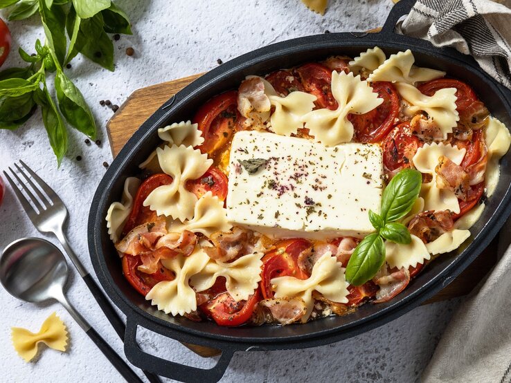 Eine schwarze Auflaufform mit der Feta-Pasta mit Speck auf grauem Untergrund.