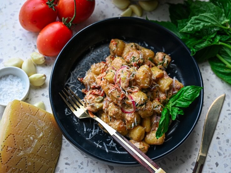 Schnitzeltopf mit Gnocchi auf schwarzem Teller – darum herum liegen einige der Zutaten verteilt.