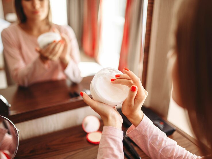 Close-up einer Frau, die mit ihren Fingern Creme aus einer Cremedose nimmt. 