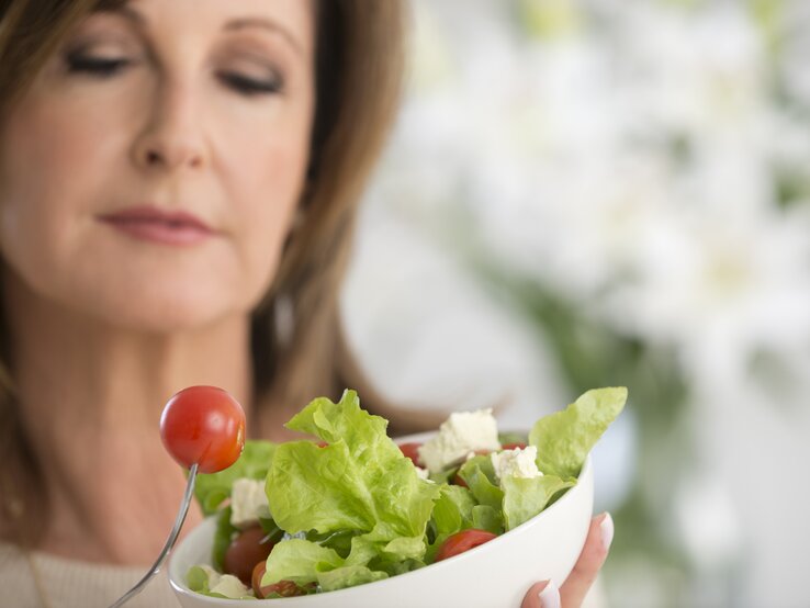 Frau mit einer Salatschale in der Hand beäugt kritisch eine kleine Tomate. 