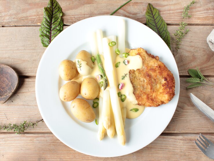 So schmeckt der Frühling: probieren Sie unseren .Spargel mit Schnitzel in frühlingshafter Cremesoße. Spargel mit Schnitzel in frühlingshafter Cremesoße mit Kartoffeln auf Holztisch