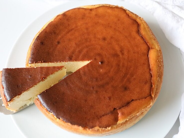 Ein weißer Teller mit dem braunen Käsekuchen auf einer weißen Tischdecke.