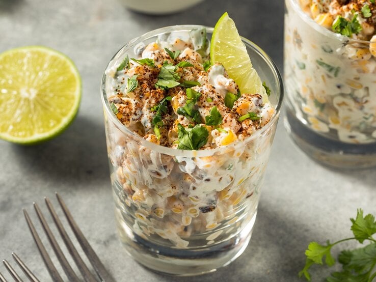 Mexikanischer-Thunfischsalat Zwei Gläser mit dem Salat auf einem grauen Untergrund. Daneben eine Limettenhälfte und ein paar Korianderzweige.
